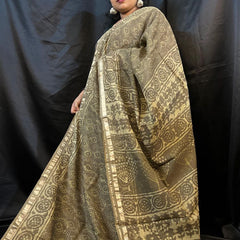 Woman wearing a traditional gold and black patterned saree against a black background