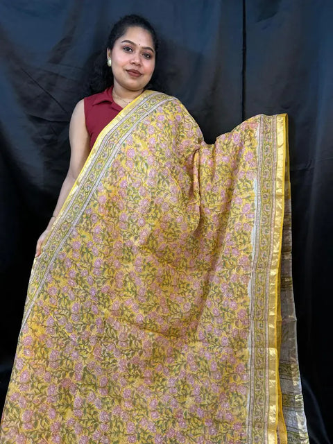 Woman wearing a yellow saree with a floral pattern against a black background