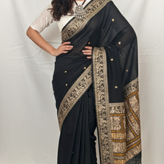 Woman wearing a black saree with gold patterns against a white background