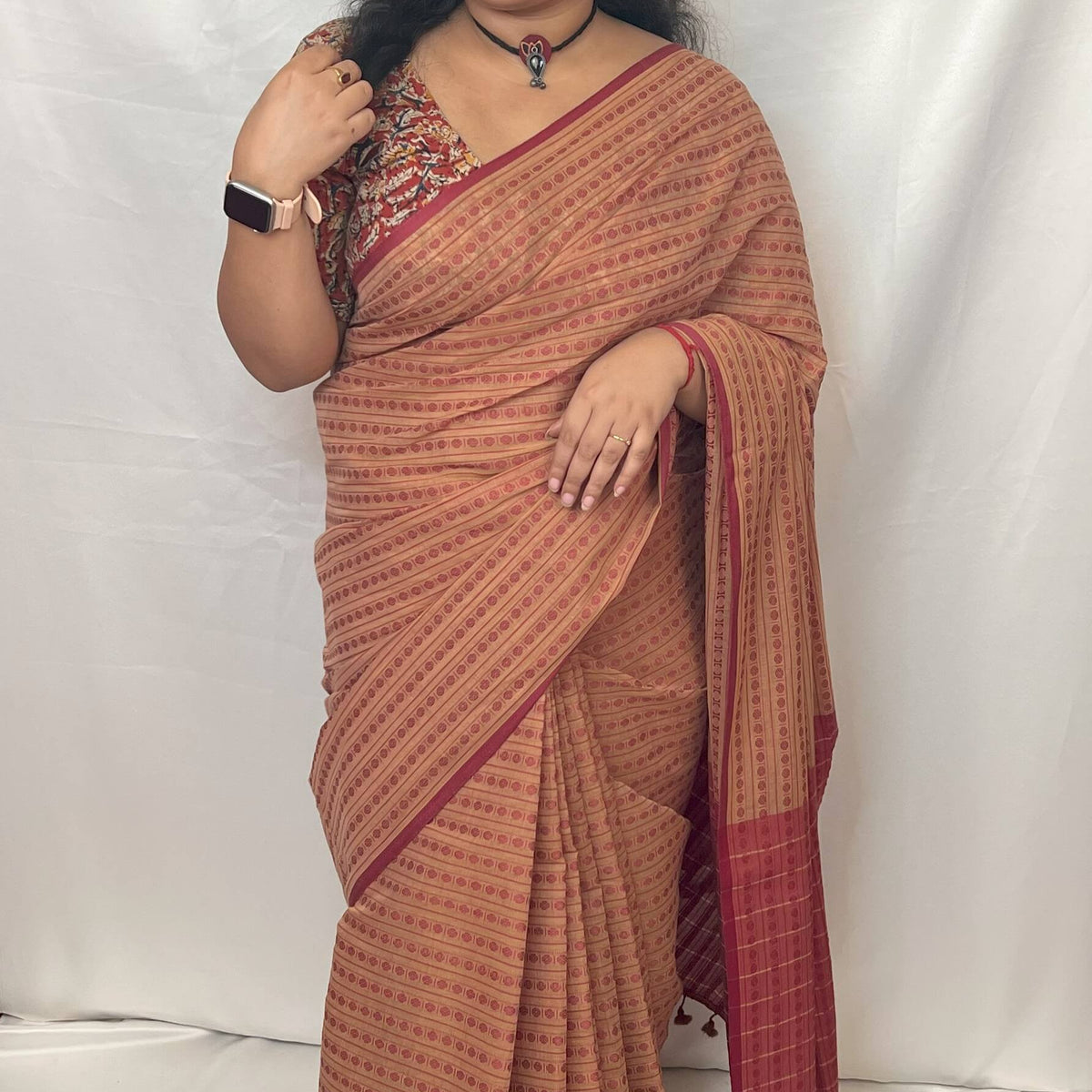 Woman wearing beige cotton handloom saree with red motifs.