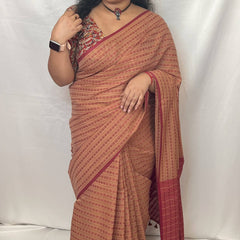 Woman wearing beige cotton handloom saree with red motifs.