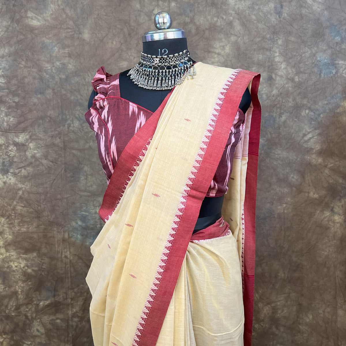 Mannequin wearing a beige and red saree with a matching blouse against a textured brown background