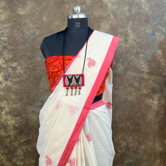 White saree with red border and red blouse on a mannequin against a textured brown background